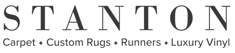 Logo for Stanton featuring the brand name in a large, elegant, all-caps serif font. Below it, the words "Carpet", "Custom Rugs", "Runners", and "Luxury Vinyl" are listed in a smaller sans-serif font, each separated by a small diamond symbol.