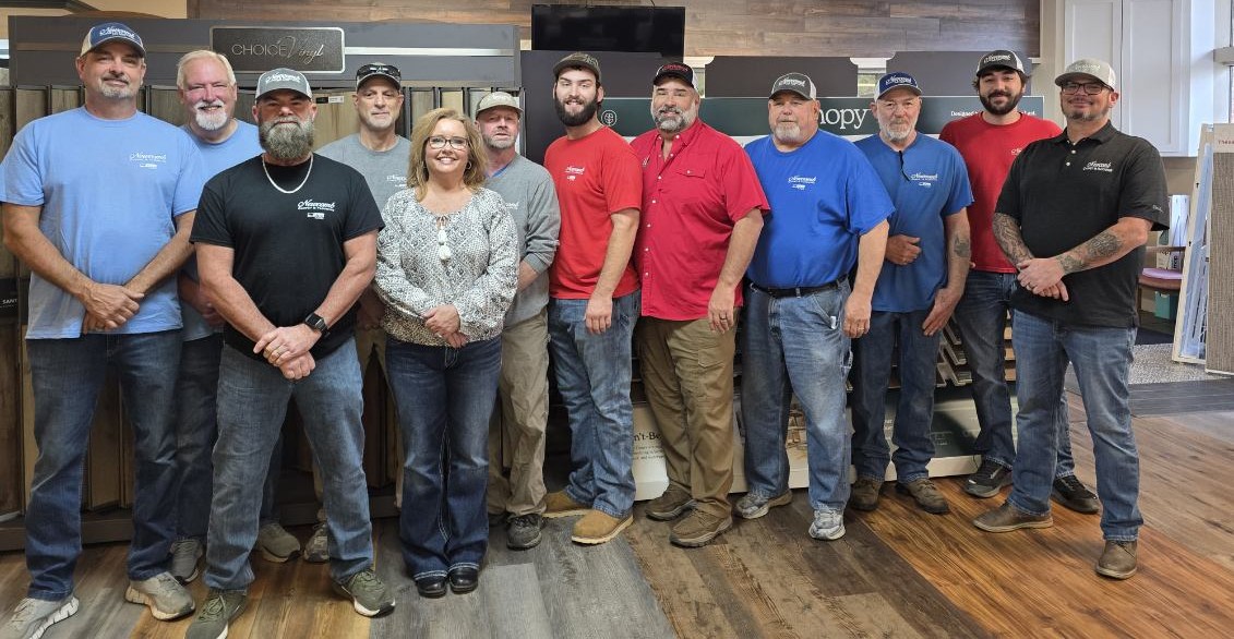 Group photo of the flooring team standing in a showroom in front of "Choice Vinyl" and "Canopy" hardwood and luxury vinyl plank displays.